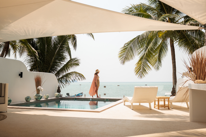 Luxurious beachfront pool with palm trees and a woman enjoying a tropical vacation, highlighting lifestyle upgrades such as travel, funded by accessing home equity in Canada.