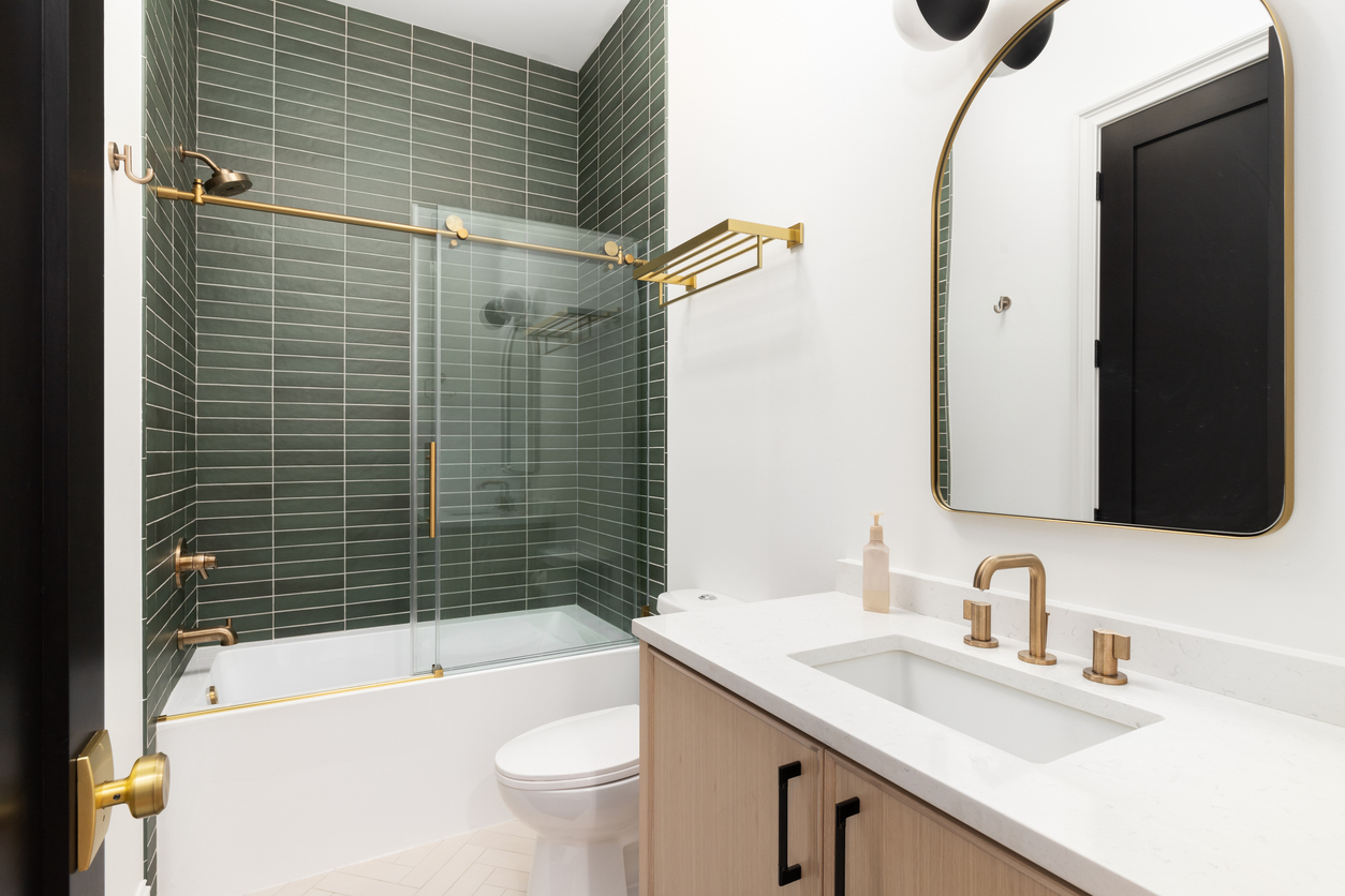 Contemporary bathroom with a sleek design, featuring a glass shower enclosure, green tile walls, and gold fixtures, ideal for adding value to homes in Oak Ridges and the GTA.