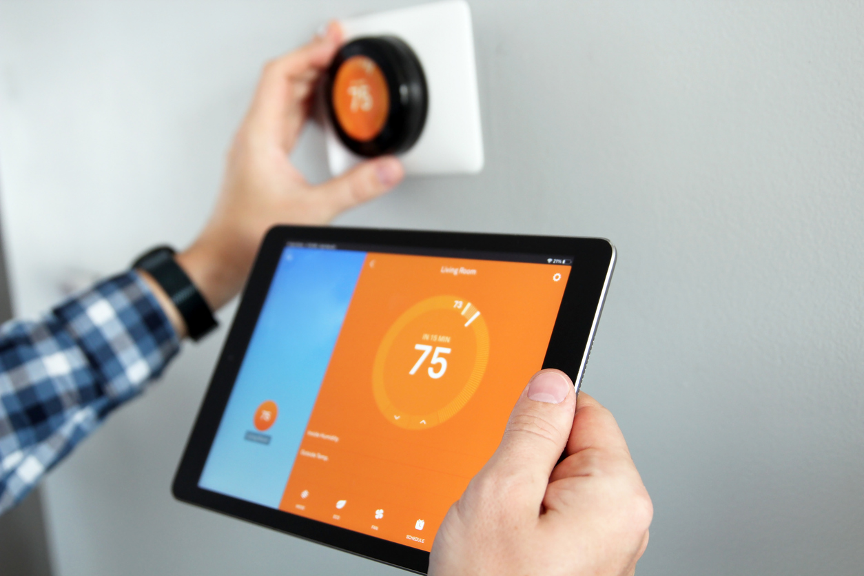 Hands adjusting a smart thermostat using a tablet, showcasing energy-efficient home upgrades that can reduce utility costs in Oak Ridges and the Greater Toronto Area.